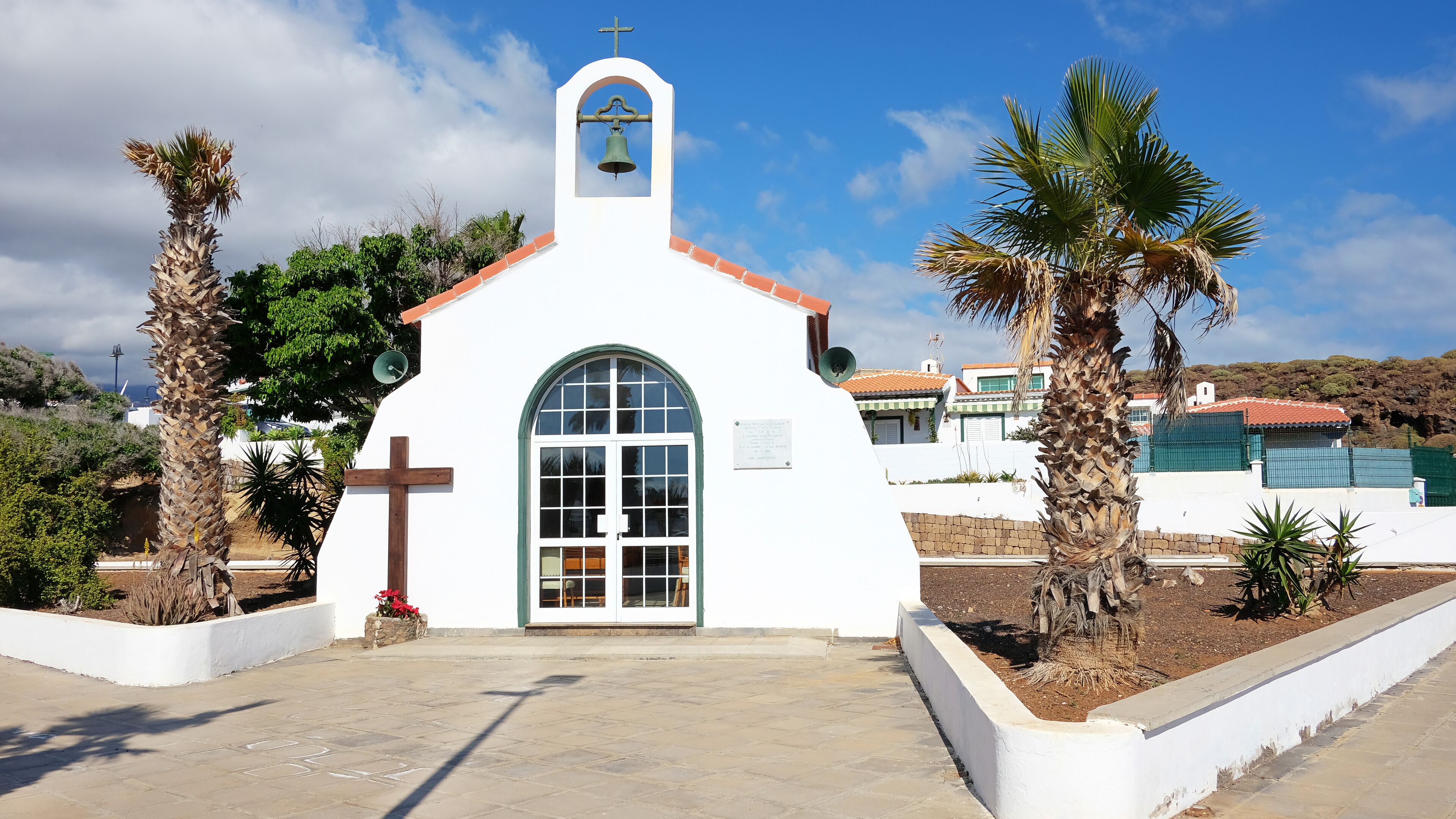 A small white church with a bell tower, palm trees, and a clear blue sky.