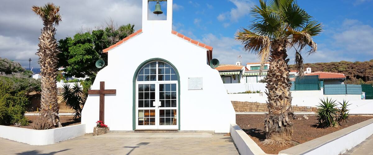 A small white church with a bell tower, palm trees, and a clear blue sky.