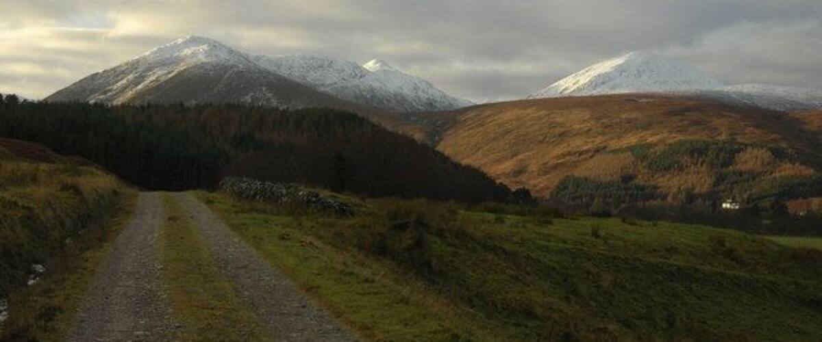 A gravel road leading to a mountain with snow-capped peaks.