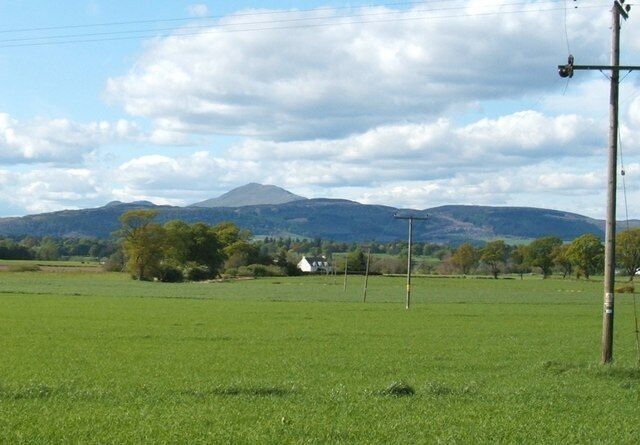 A green field with a mountain in the background and a white house.