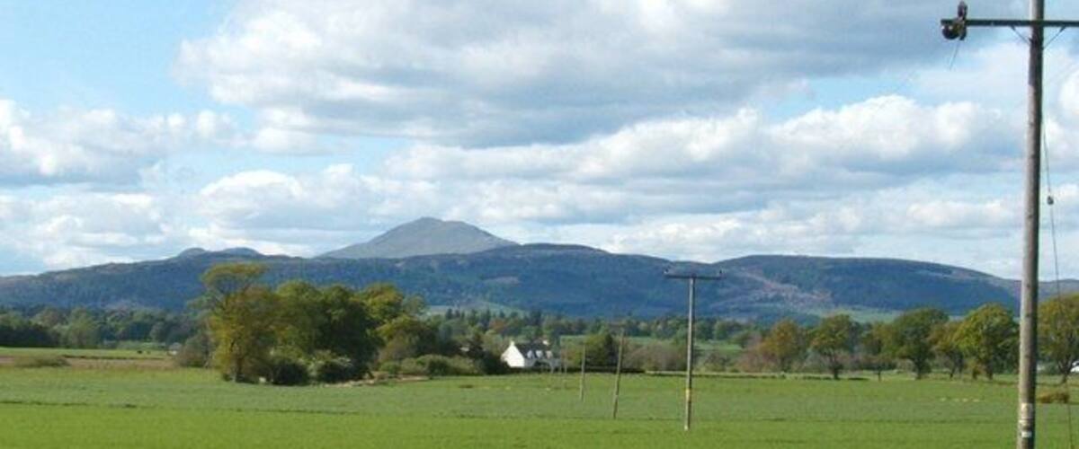 A green field with a mountain in the background and a white house.