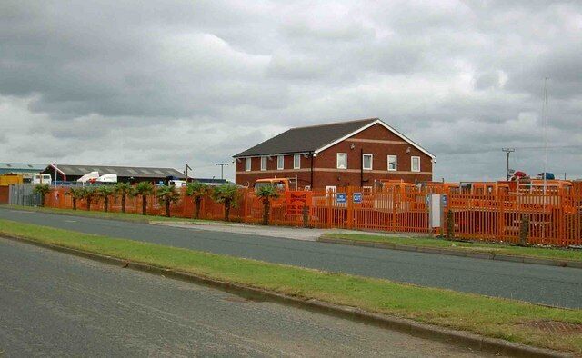 A red brick building with a grey roof, surrounded by orange construction fencing.