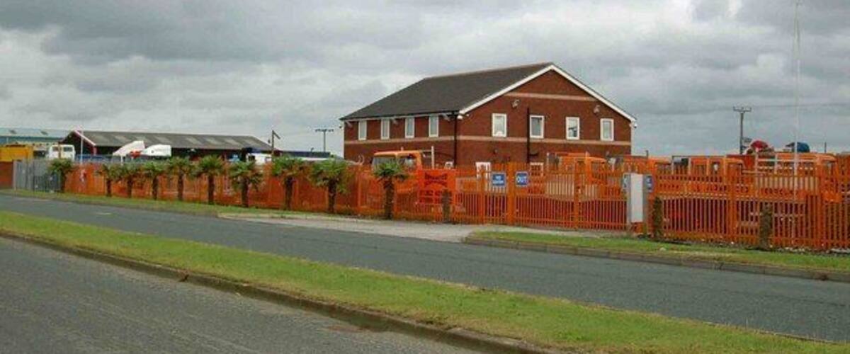 A red brick building with a grey roof, surrounded by orange construction fencing.