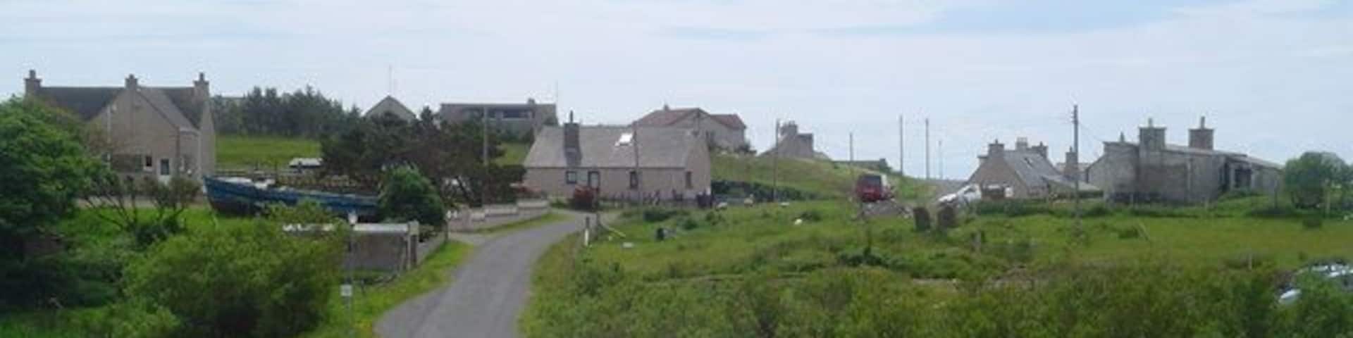 A rural road winding through a village with houses and fields.