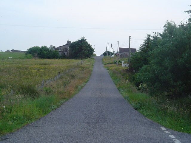 A rural road flanked by fields and houses.