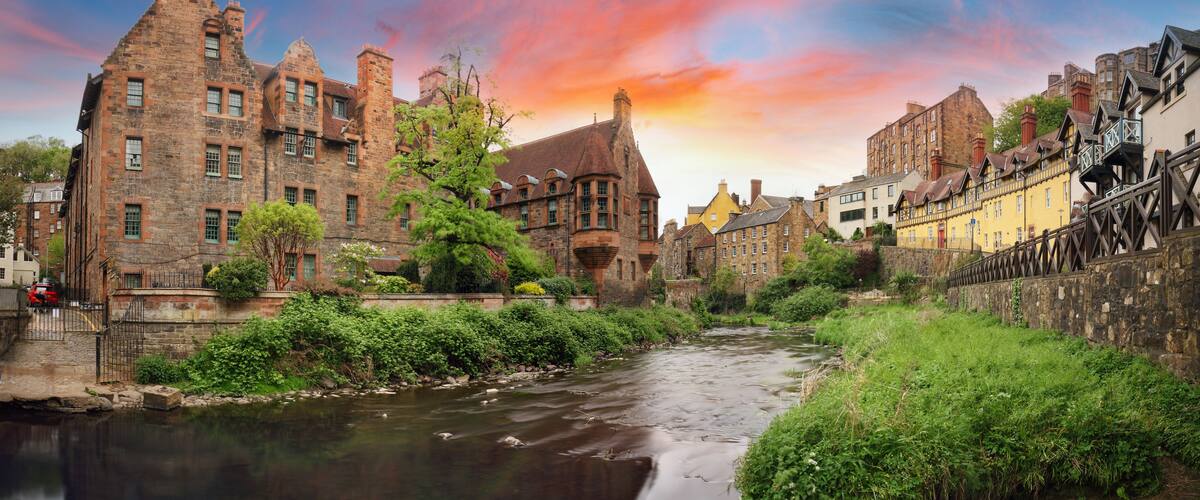 A historic town with a river, traditional buildings, and a sunset sky.
