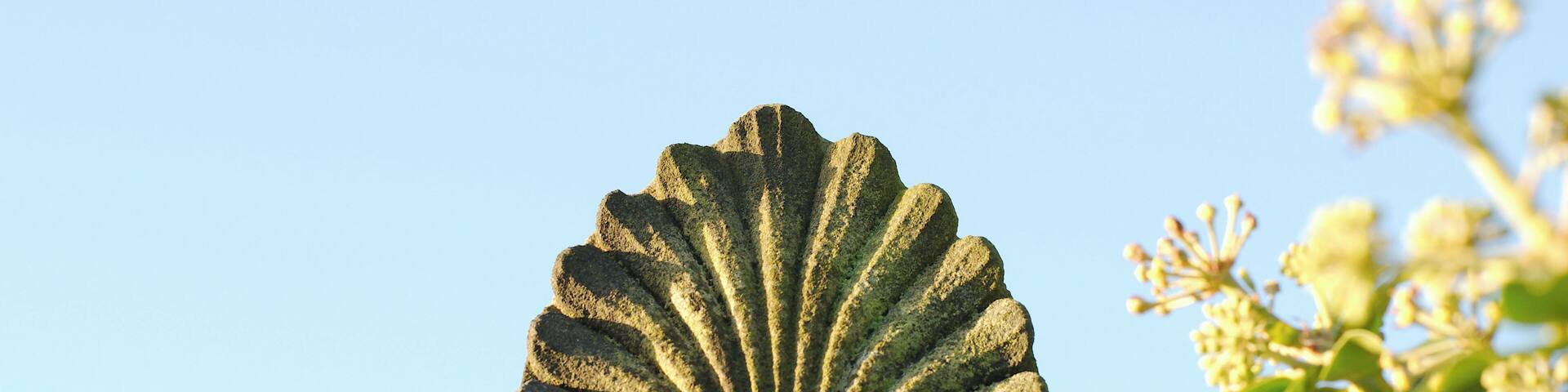 A stone sculpture of a scallop shell with intricate carvings, set against a clear blue sky.