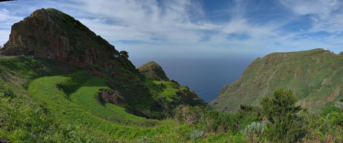 A mountainous landscape with a valley and a view of the ocean.