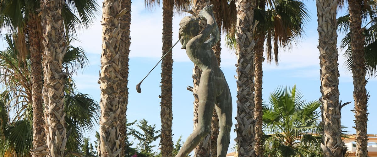 A statue of a man holding a fish in a tropical setting with palm trees.