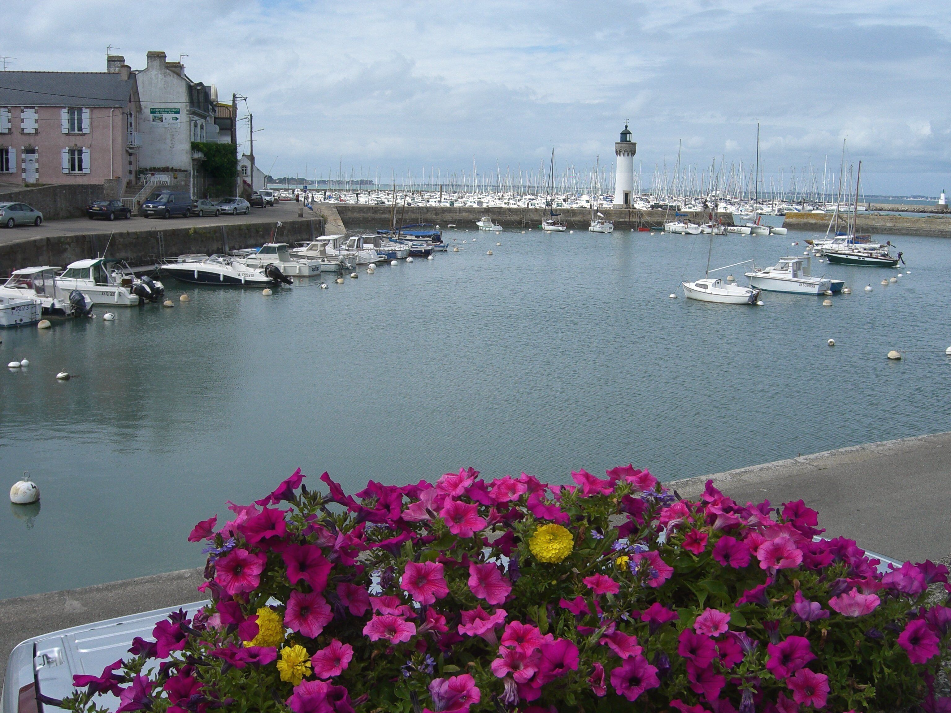 A harbor with numerous boats docked, a lighthouse, and a building with a pink facade.