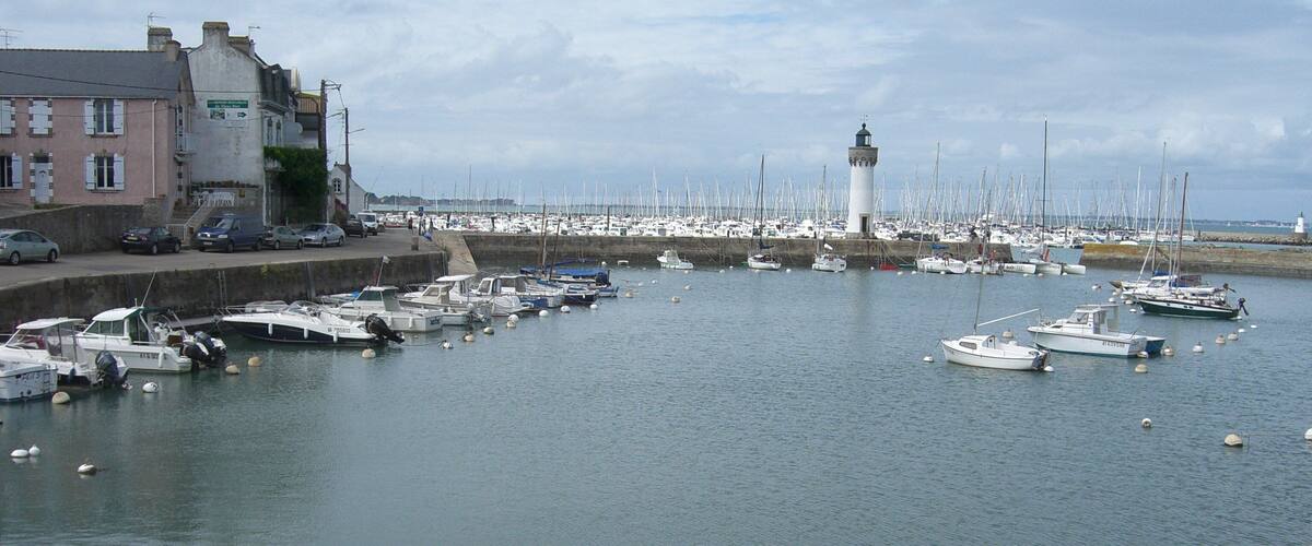 A harbor with numerous boats docked, a lighthouse, and a building with a pink facade.