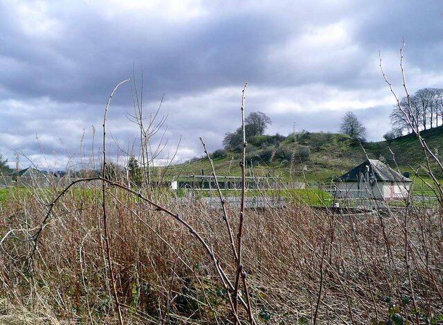 A rural landscape with a fence, a small building, and a hill in the background.