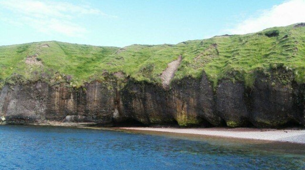 Cliff Undercutting at Roisinis. This picture, taken from a rocky outcrop, shows extensive undercutting of the cliffs. Cliff erosion is a major problem in the local area but this photograph depicting the erosion along with the blue sea and grass creeping down the cliff shows the damage as attractive rather than destructive.