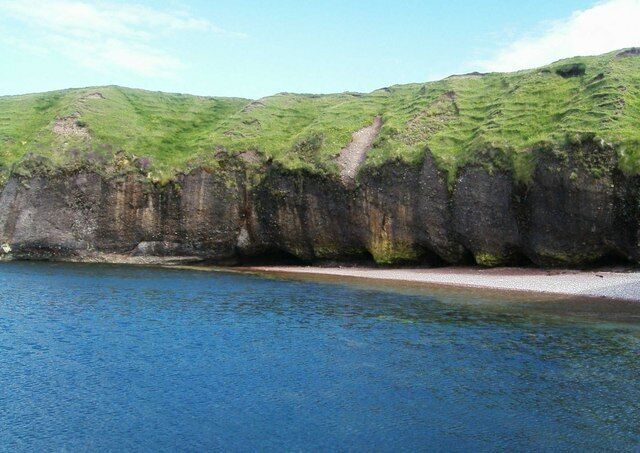 A coastal landscape with a grassy hill and a rocky cliff by the sea.