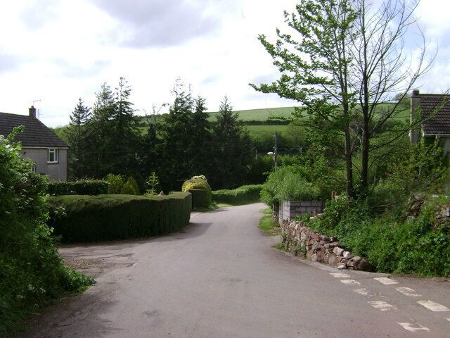 A narrow rural road flanked by houses and lush greenery.