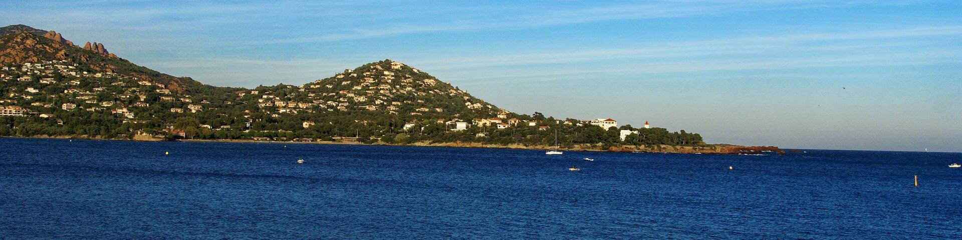 A coastal town with a hill, houses, and boats on the water.