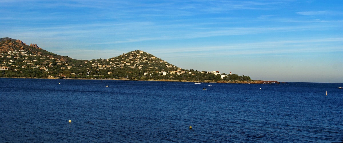 A coastal town with a hill, houses, and boats on the water.