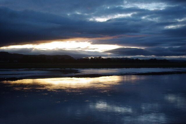 A sunset over a calm body of water with a cloudy sky.