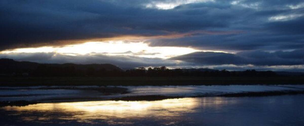 A sunset over a calm body of water with a cloudy sky.