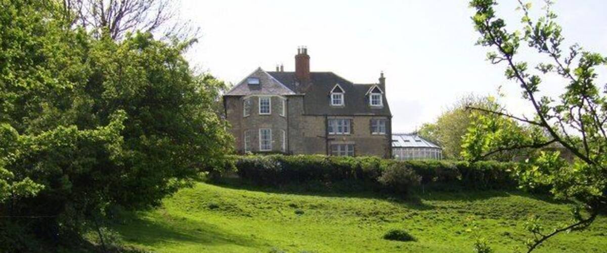 A large house on a grassy hill with a tree in the foreground.