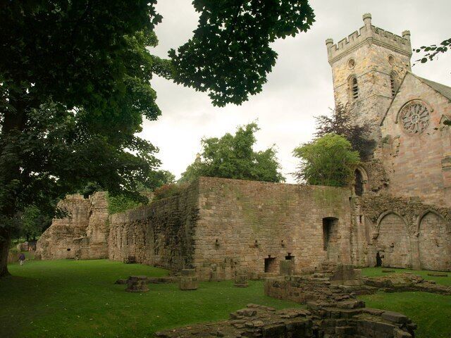 An ancient stone structure with a tower and circular window, surrounded by grassy areas and trees.