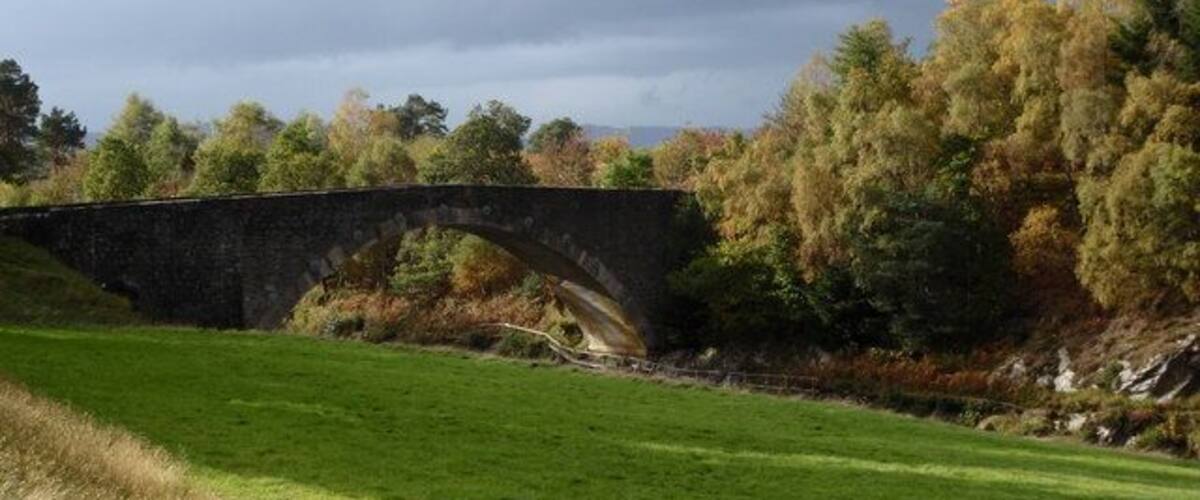 A stone bridge over a river, surrounded by autumn foliage and grassy banks.