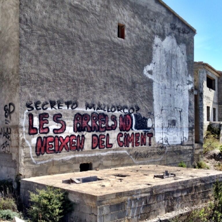 A building with graffiti that reads "SECRETO MALLORCO LES ARRELS ND NEIXEN DEL CIMENT".