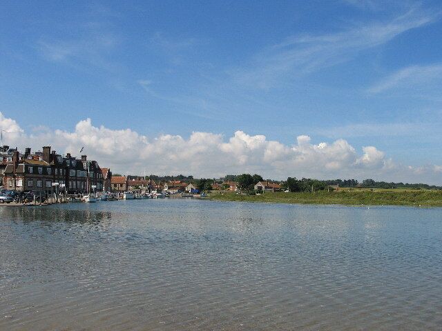 A riverside town with buildings along the water, a clear sky, and a distant green landscape.