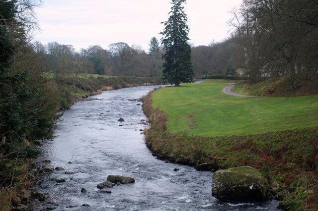 A river flowing through a rural landscape with a grassy field and trees.