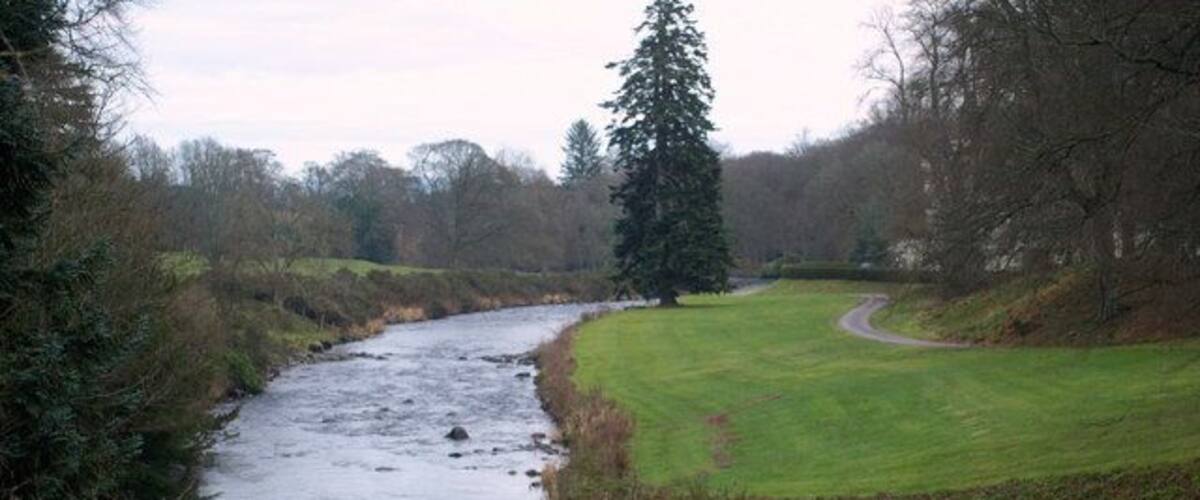 A river flowing through a rural landscape with a grassy field and trees.