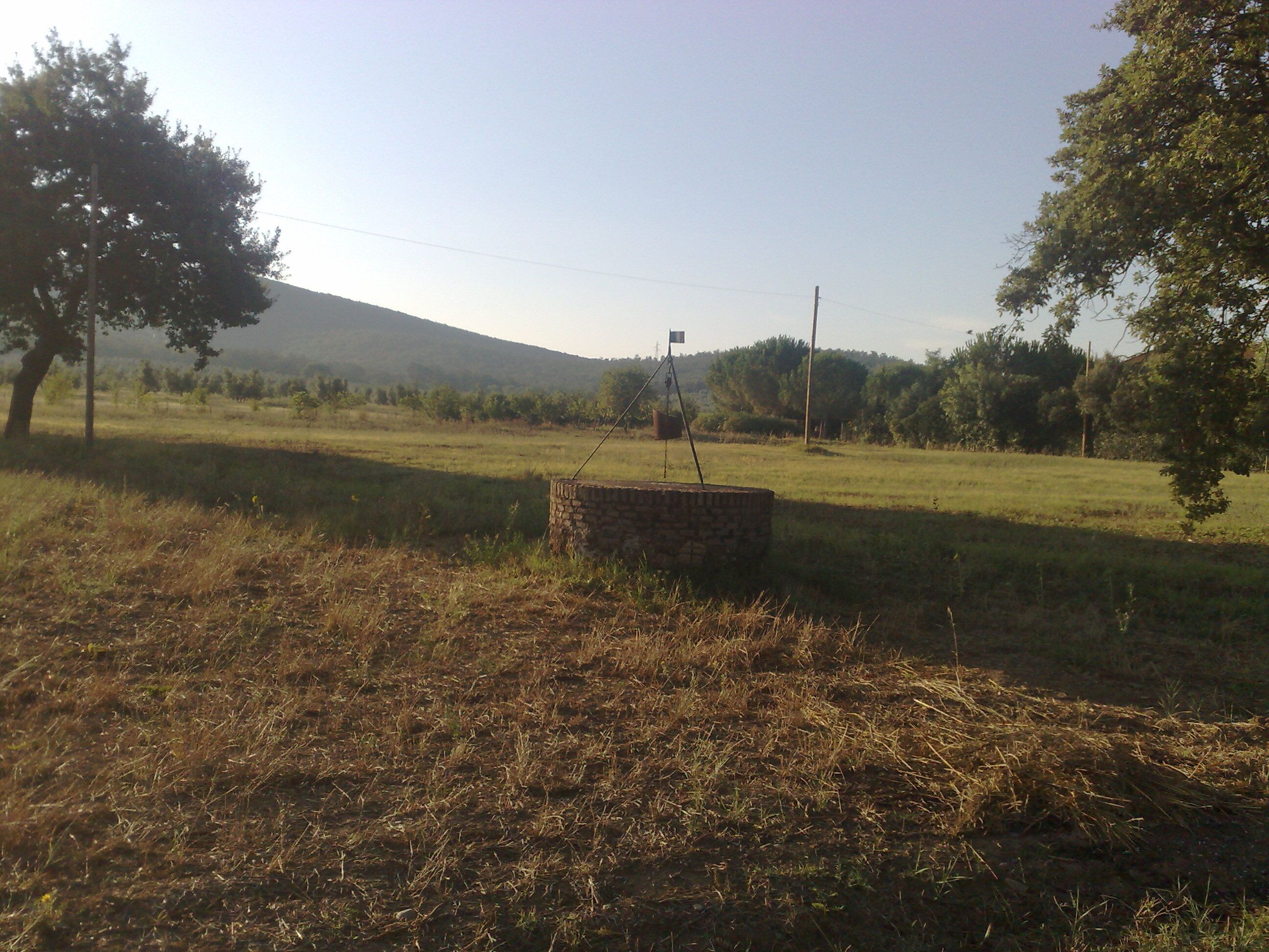 A rural landscape with a stone structure, trees, and a distant hill.