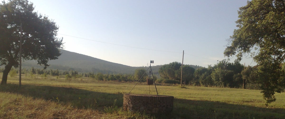 A rural landscape with a stone structure, trees, and a distant hill.