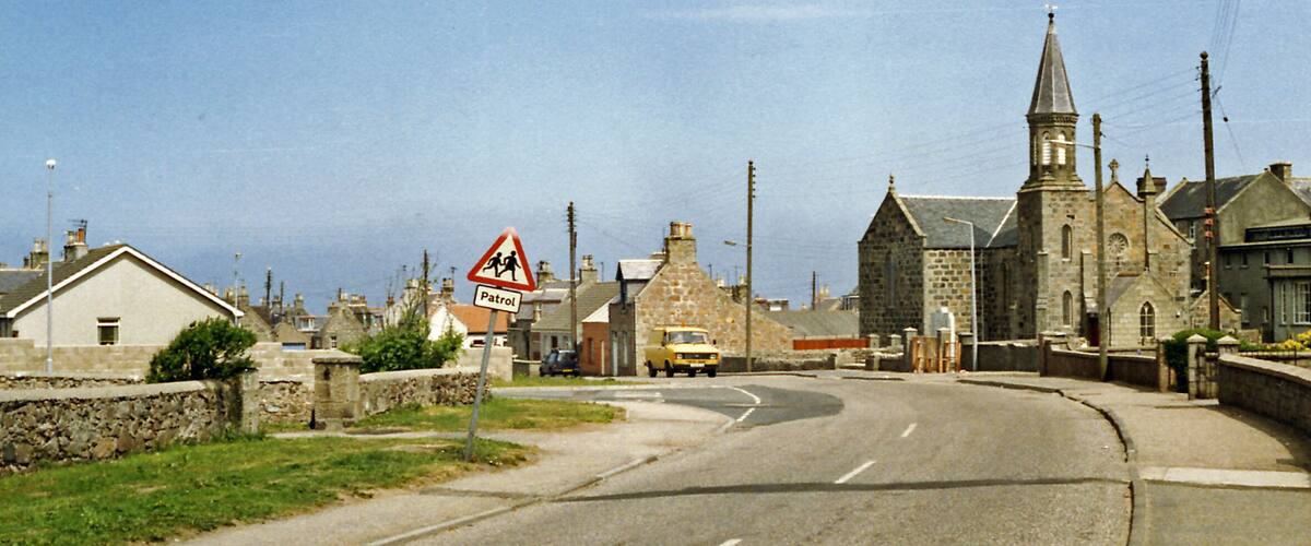 A rural road with a church, a 'Patrol' sign, and a 'School Crossing' sign.