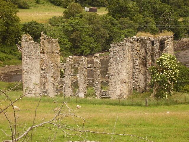 A ruined stone structure in a grassy field with trees in the background.