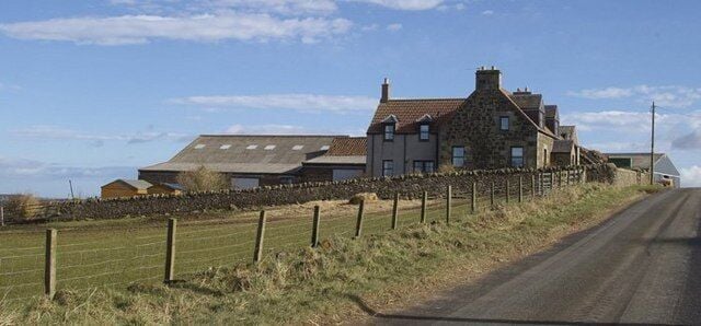 A rural road with a stone house and a stone wall on the left.