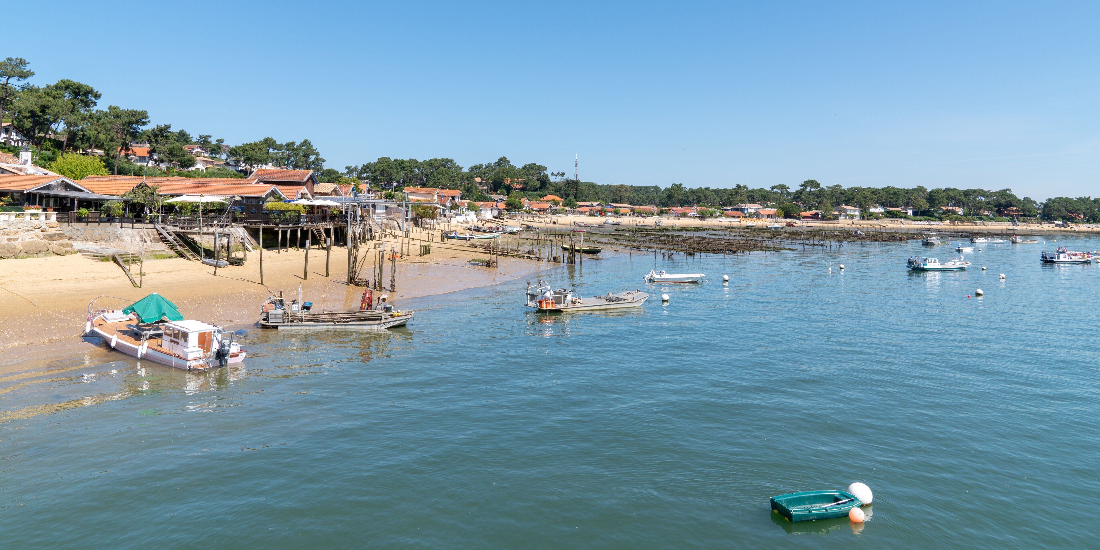 A coastal town with boats docked at the pier, sandy beach, and houses with red roofs.