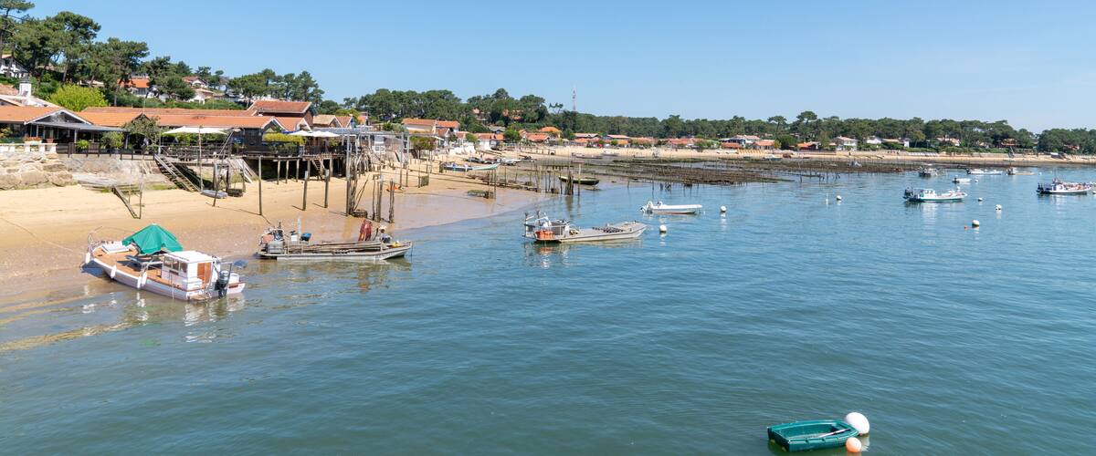 A coastal town with boats docked at the pier, sandy beach, and houses with red roofs.