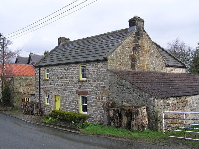 A stone house with a sloped roof, a yellow door, and a large tree stump in front.