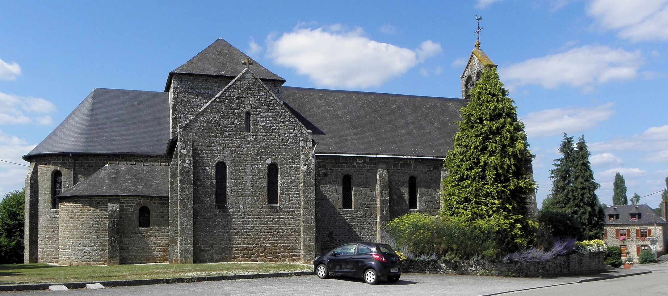 A stone church with a tall bell tower and ivy-covered trees.