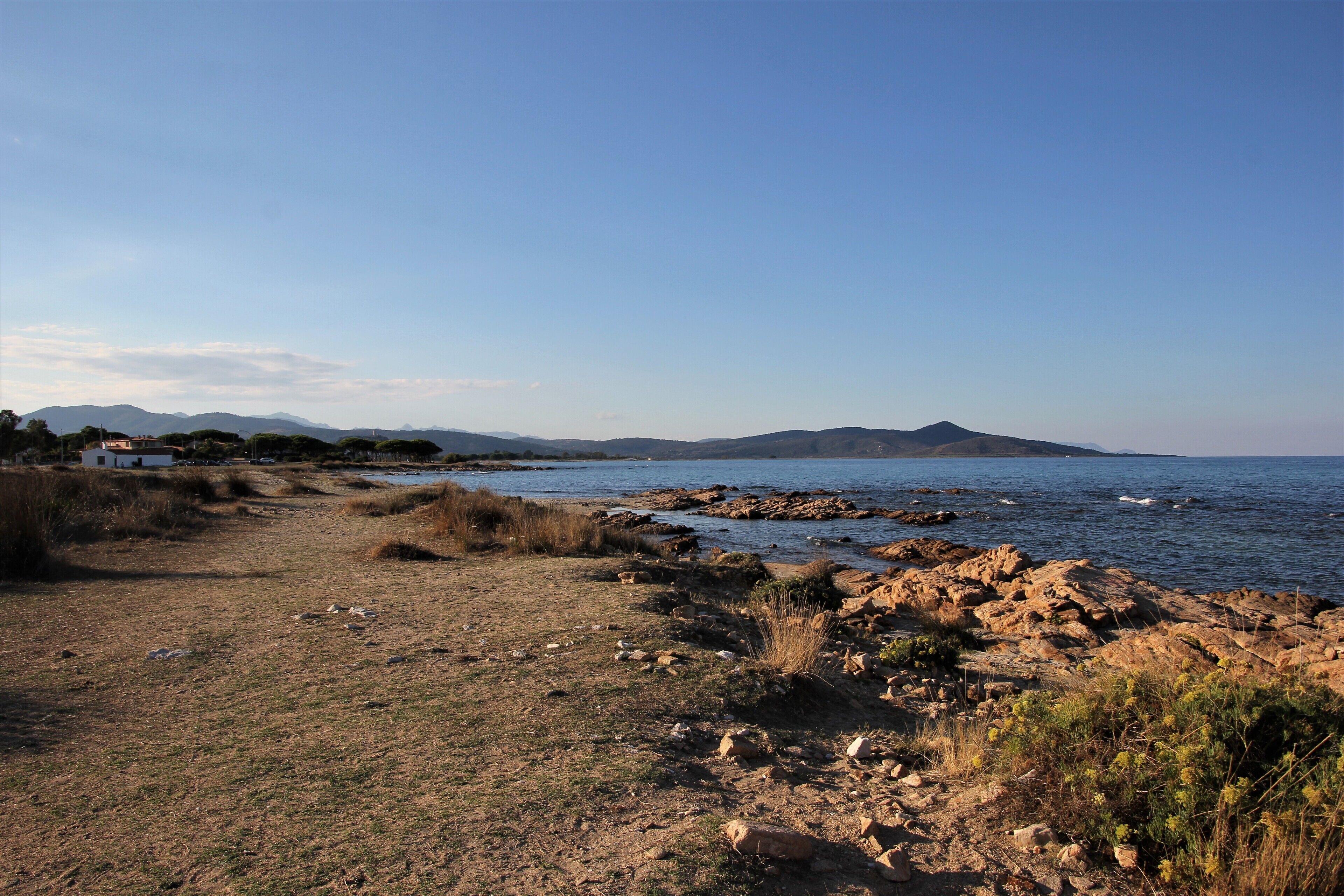 A rocky shoreline with a clear path leading to a body of water, surrounded by hills and sparse vegetation.