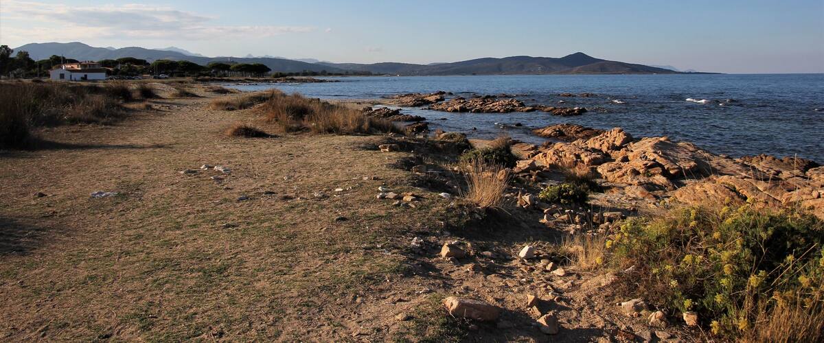 A rocky shoreline with a clear path leading to a body of water, surrounded by hills and sparse vegetation.