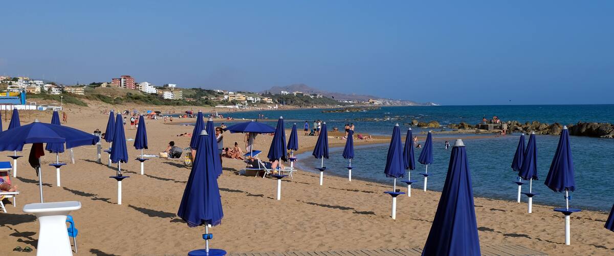 A beach with rows of blue umbrellas and lounge chairs.