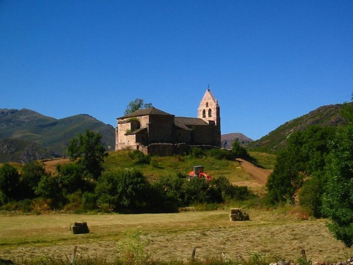 A historic stone church with a bell tower on a hillside.