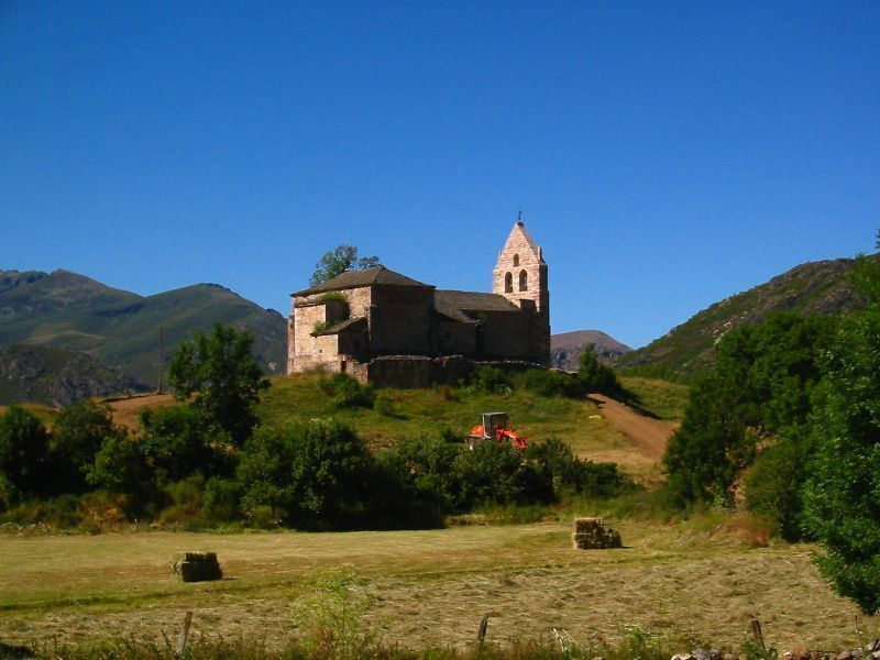 A historic stone church with a bell tower on a hillside.