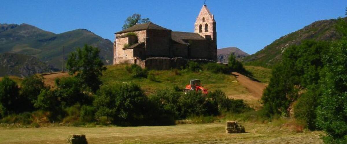 A historic stone church with a bell tower on a hillside.
