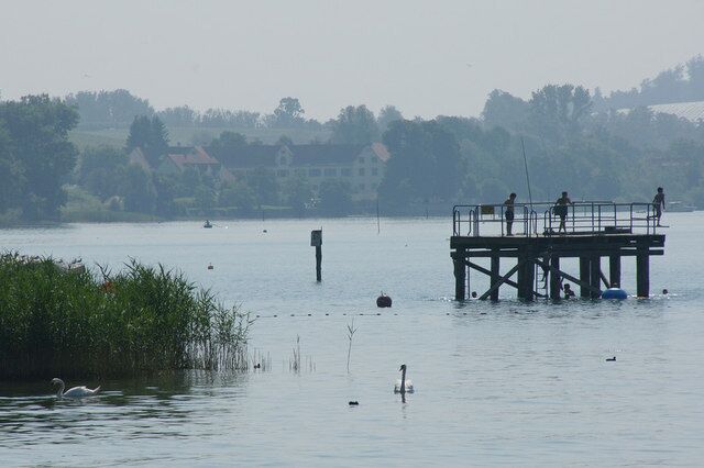 A pier extending into a calm lake with a few people standing on it.