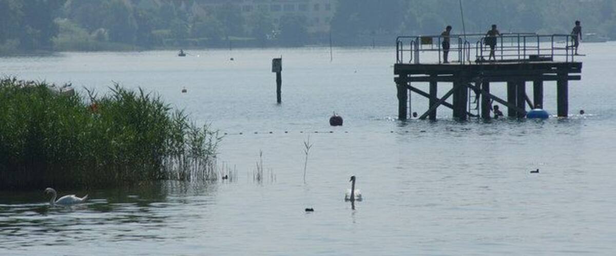 A pier extending into a calm lake with a few people standing on it.