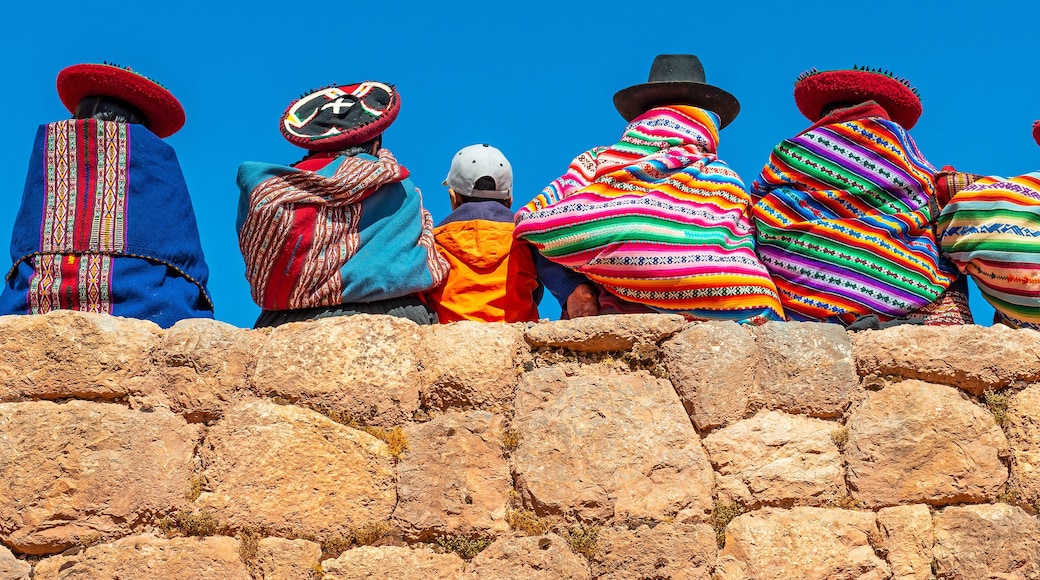 Panoramic photograph of Quechua indigenous women in traditional clothing with a boy sitting on an ancient Inca wall in Chinchero, Cusco Province, Peru.