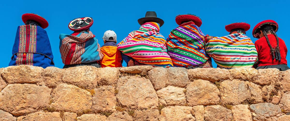 A group of people in traditional colorful attire standing on a stone wall.