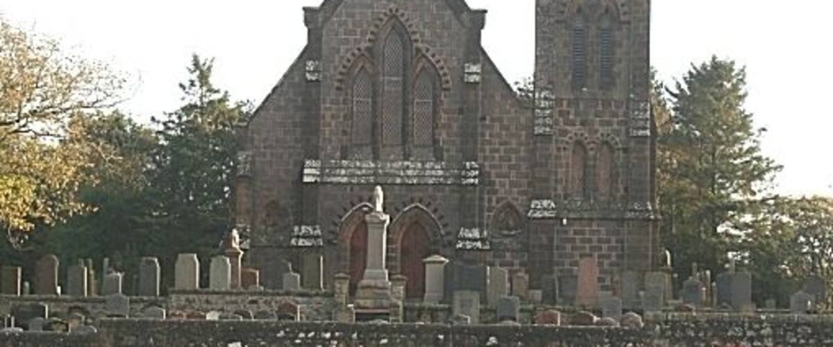 A church with a tall spire and a stone wall with gravestones.